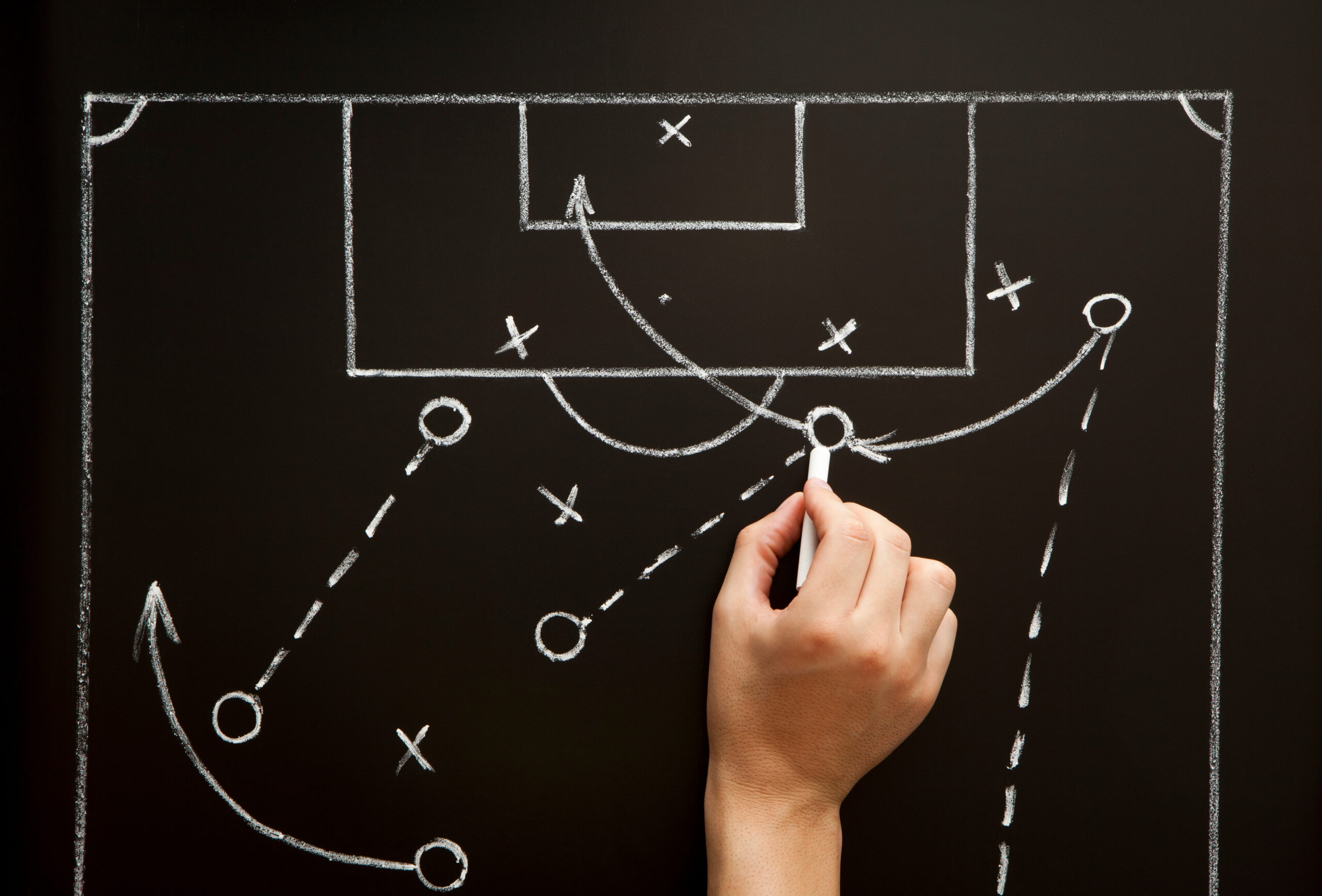 Man drawing a soccer game strategy with white chalk on a blackboard.